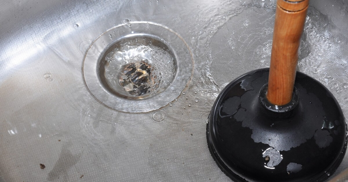 a black plunger with a wooden handle is in a sink