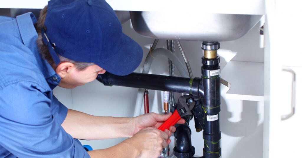 a plumber works on a pipe under a sink