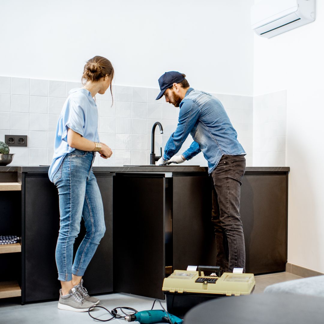 Schedule With a Maintenance Plumber a man and a woman are working on a kitchen sink .