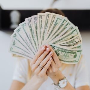 Woman holding multiple $20 bills in front of her face. 