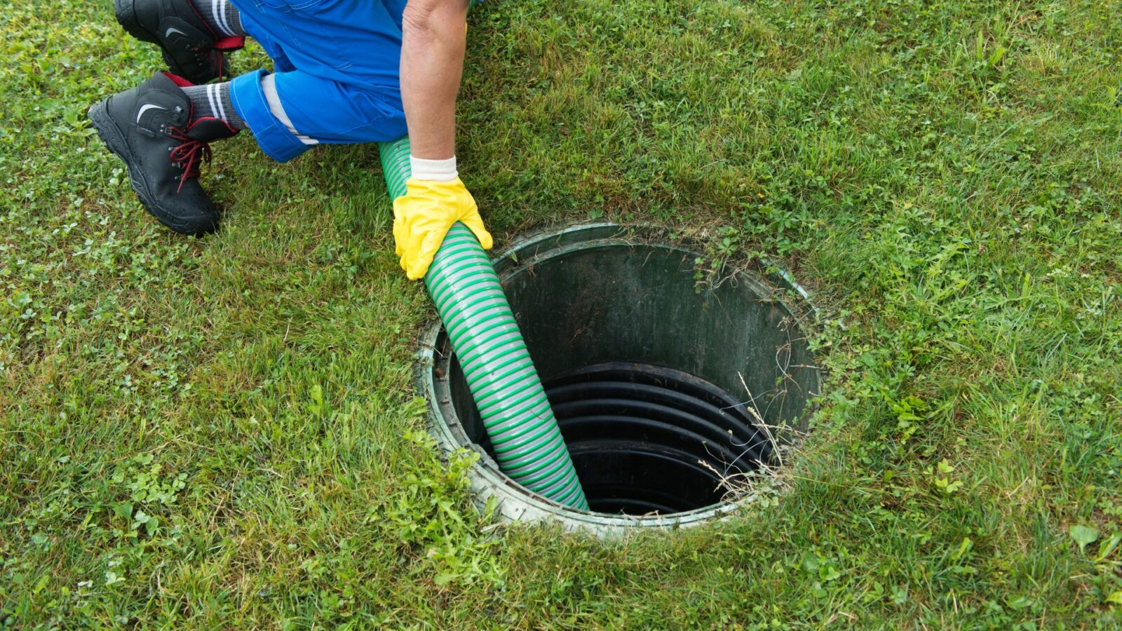 a man wearing yellow gloves is pumping water into a septic tank
