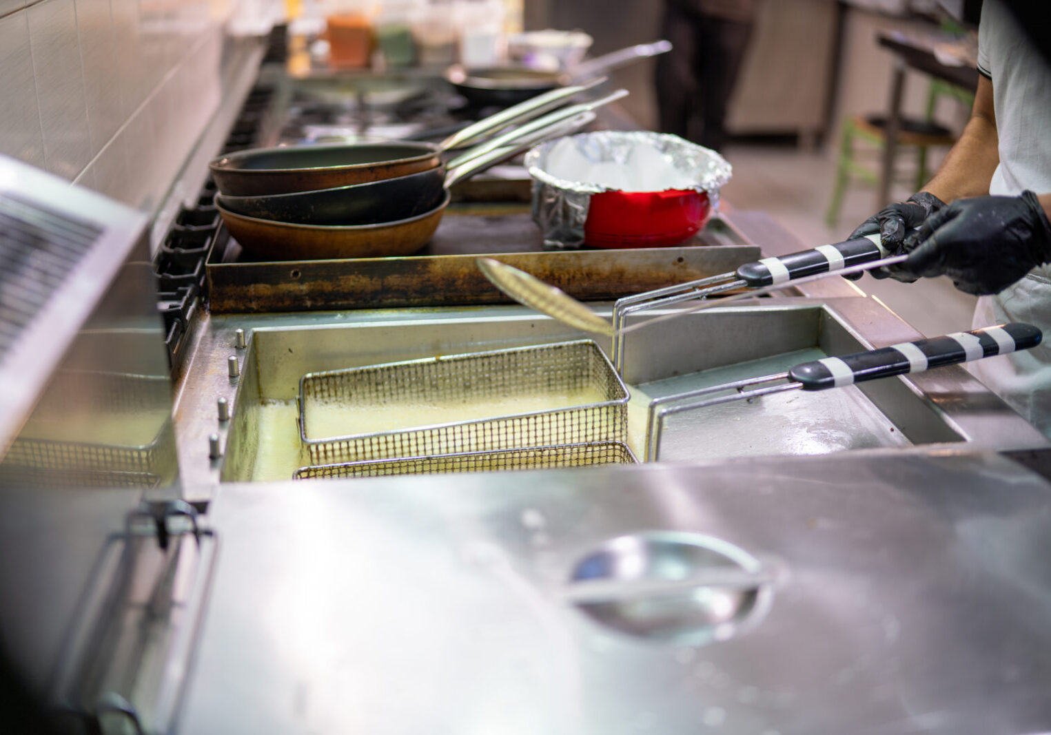 Metal basket lifting crispy fried food from bubbling oil inside a deep fryer, showcasing the vibrant atmosphere of a professional kitchen specializing in Indian cuisine